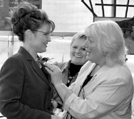 Charlotte Jewell pins a flower corsage on the governor as Kathy Hosford watches