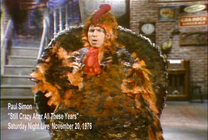 Paul Simon singing earnestly in a turkey suit