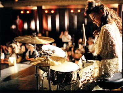 Meg White on stage playing drums in a white dress
