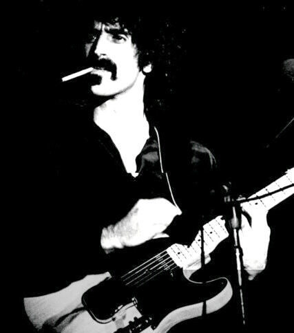 Frank Zappa on stage smoking a cigarette and playing guitar