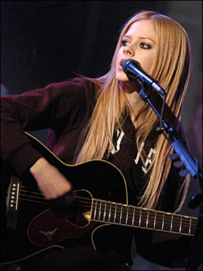 Avril Lavigne sitting down playing acoustic guitar